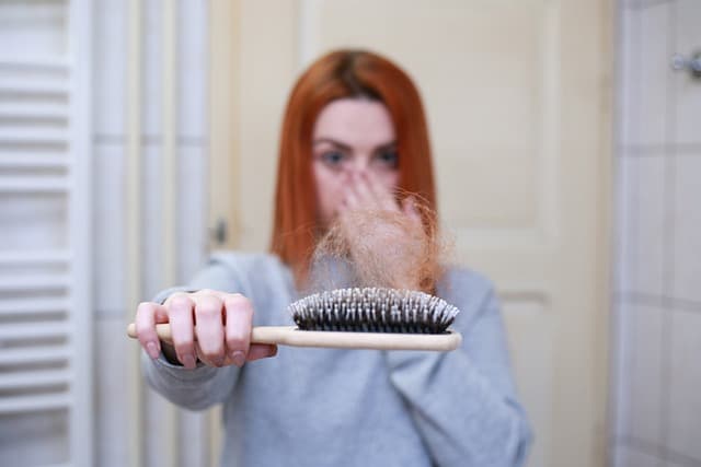 A Red-Headed Woman Holding a Brush With Her Hair In It