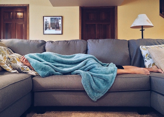A Sick Person Laying Under a Blanket on a Sofa