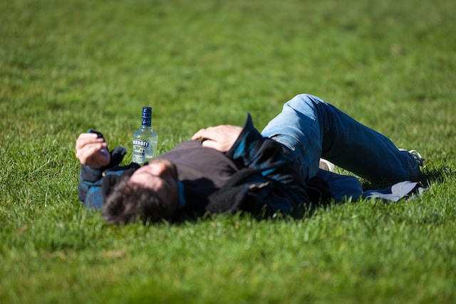 a man passed out on a grass field next to a bottle of vodka