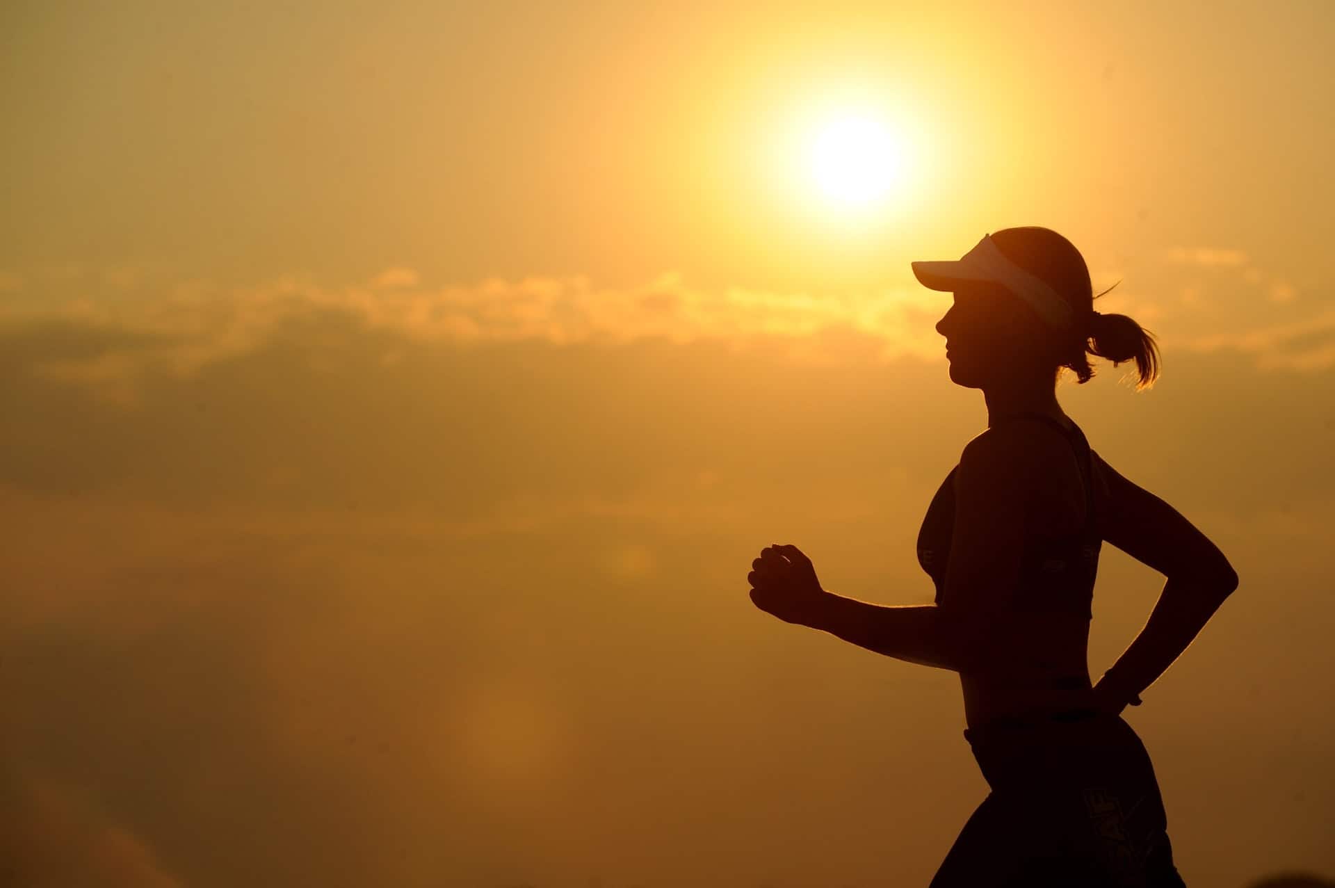 a woman running with the sun setting in the background