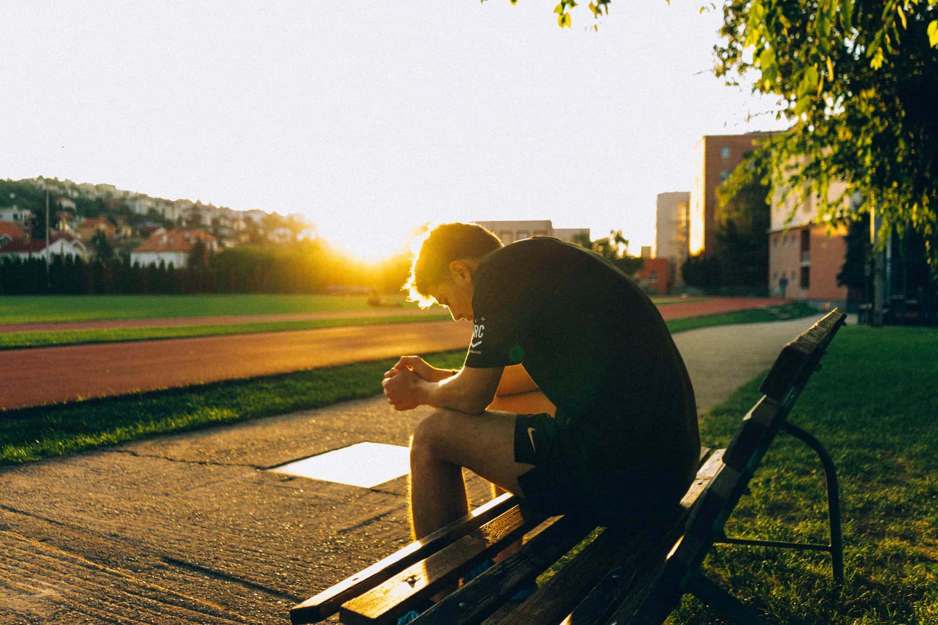 a man sitting on a park bench and catching his breath while the sun sets