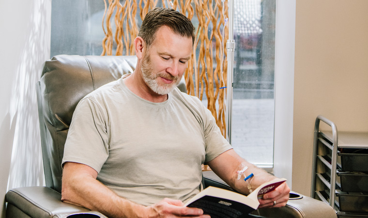 Man getting an NAD IV treatment, reading a book to pass the time looking relaxed