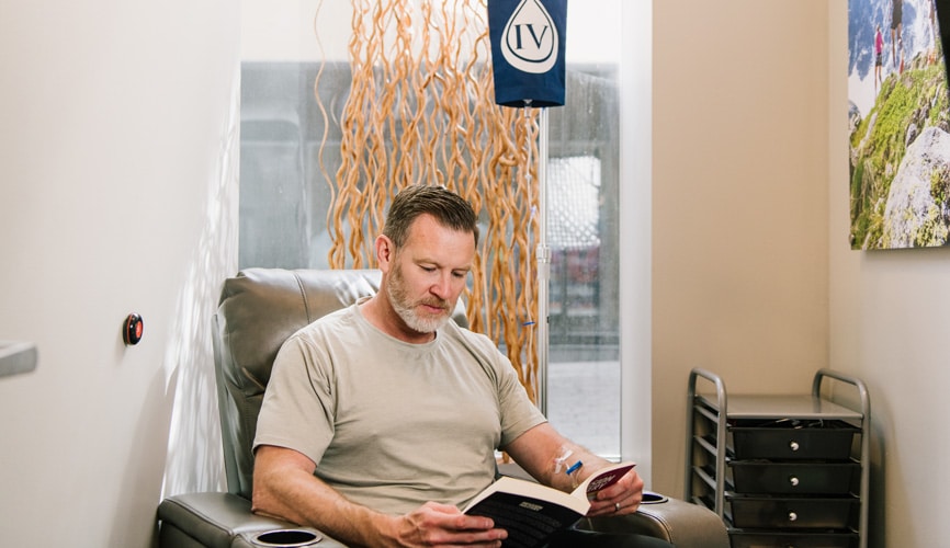 Man receiving NAD+ infusion therapy reading a book in a quiet, private room