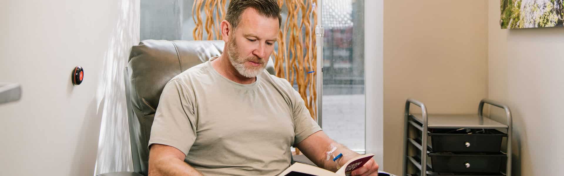 Man receiving NAD+ infusion therapy reading a book in a quiet, private room