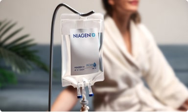 IV therapy drip bag on a stand beside a seated person receiving treatment.